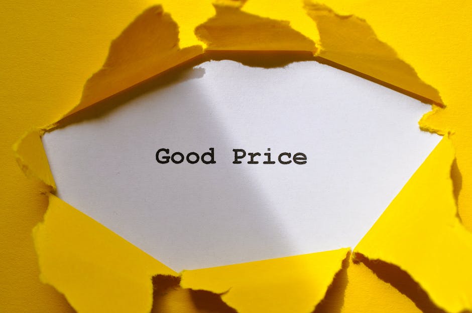 A close-up view of a bright yellow paper surface with a tear in the paper revealing a white inner layer. Inside the torn area, the words 'Good Price' are printed in black text on a white background. The tearing creates a jagged edge around the opening, emphasizing the contrast between the yellow outer layer and the white inner layer with the printed message. The image highlights a visual metaphor related to cost or value, which can be associated with household removals and moving services provided by Man with Van Ilford, as seen in the context of house relocation and furniture transport, with the focus on affordability and transparent pricing.